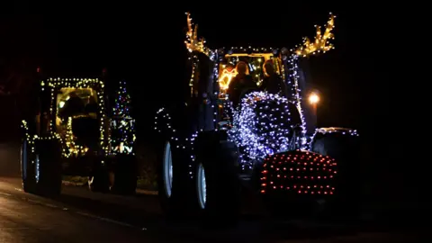 South Staffs Water Two tractors covered in an array of festive fairy lights in the middle of a road.