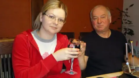 Yulia Skripal sits next to her father Sergei at a table with a glass of wine