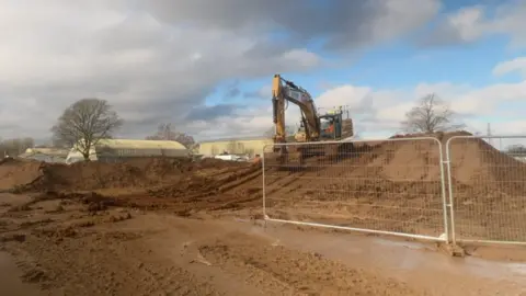 A building site near the Culham campus. The picture shows piles of mud, with a large yellow vehicle scooping earth onto one of the piles. The site will eventually form part of a new Clifton Hampden bypass. 