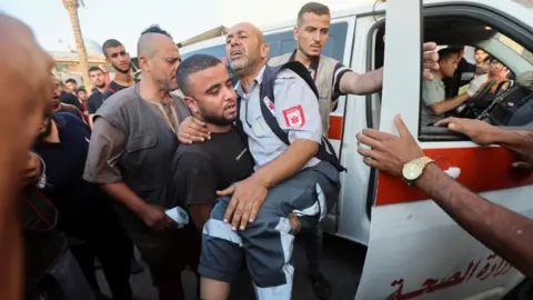Reuters A man carries an injured Palestinian paramedic in Deir al-Balah, in the central Gaza Strip, on June 4, 2024