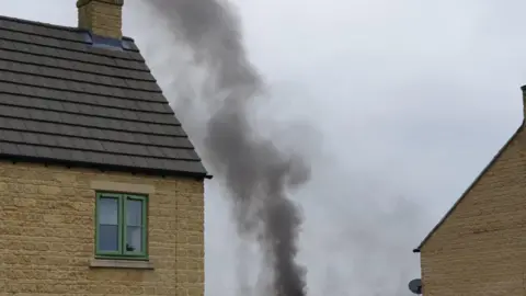 Rebecca Pass A thick plume of black smoke pictured next to a house