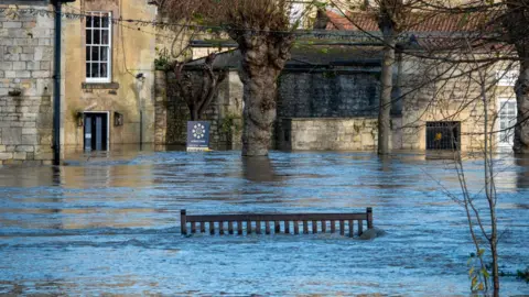 Getty Images The centre of Bradford-on-Avon is seen covered in flood water, with the top of a wooden bench visible. In the background water is seen halfway up walls and doorways