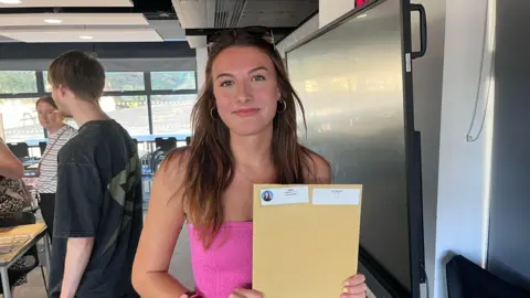 Phil Harrison/BBC A girl in a pink top holds a brown envelope.