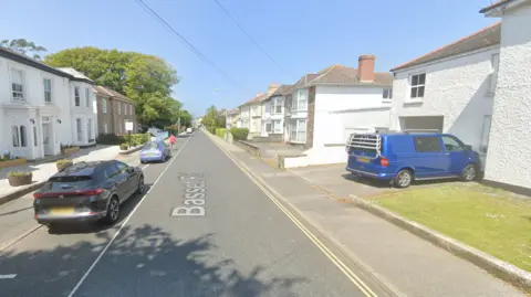 Google A Google street view Basset Road, Camborne. It's a long road with multiple houses and cars along it.