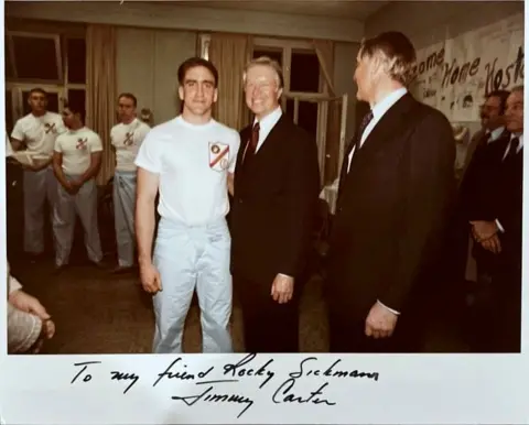 Foto yang dikirimkan Rocky Sickmann, seorang Marinir dengan piyama, berdiri di samping Presiden Jimmy Carter sementara yang lain melihatnya