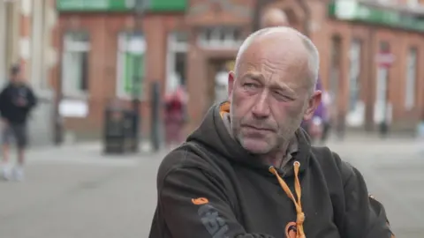 Man in black hoodie from shoulders up, with aldershot out of focus in the background