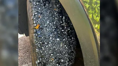 A car tyre that has been covered in small rocks and a black gooey substance. 