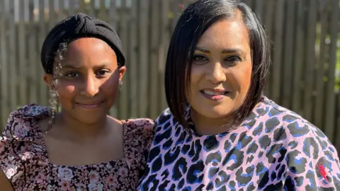 Ekta with her daughter Anisa, standing outside by a garden fence. 