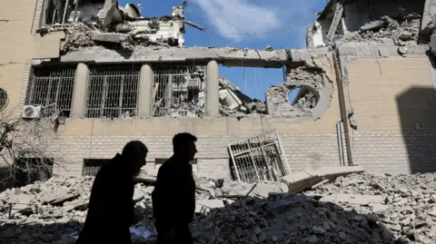 Reuters People in silhouette walk past damaged buildings