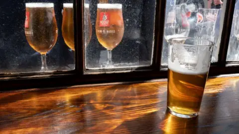 Getty Images A half-drank pint of lager sits on a bar, in the background there are three full pints