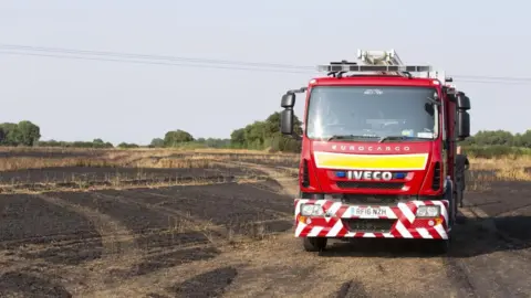 A fire engine is parked on a piece of scorched, burnt, brown farmland.