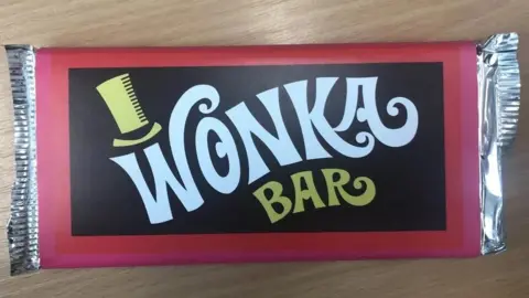 Powys County Council A chocolate bar labelled Wonka Bar with a top hat over the W and red and black packaging.