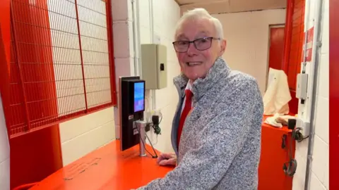 Alan seen stood behind turnstile smiling at camera