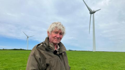 Man standing in a field in front of three wind turbines