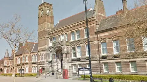 Google A three-storey brown brick building with a central entrance