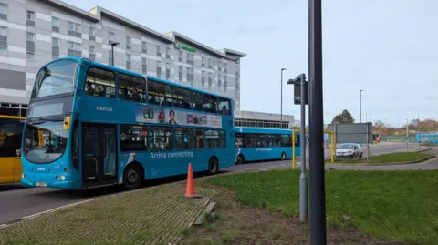 LDRS A turquoise double decker bus on a road outside of the bus station, a tall grey building.
