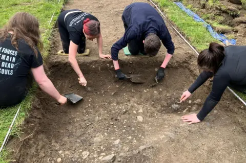 After the Festival Four people use trowels to carefully clear away soil in an area excavated at the garden festival site.