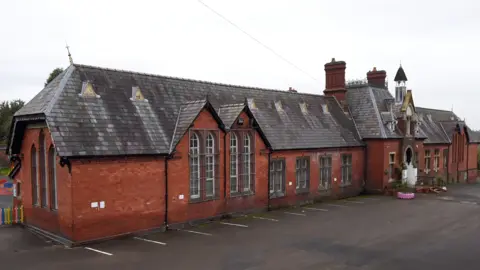 A Victorian building made out of red brick with tall pointed windows and a bell tower.