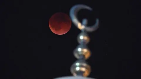 Getty Images The full moon, which has a deep dark hue, pictured above a silver minaret in Kuwait City in Kuwait. 