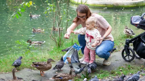 Getty Images Woman with toddler feed ducks and birds at the side of a lake 