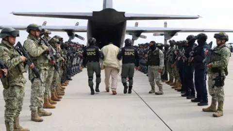 Agents of Mexico’s Secretariat of Security and Citizen Protection escort a detainee as Mexico sends another 37 alleged members of criminal organizations to the United States, at Adolfo Lopez Mateos International Airport in San Pedro Totoltepec, Mexico.