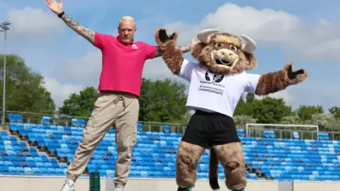 Iwan Thomas and Bab, the official mascot for the championships, jumping in the air in an empty stadium.