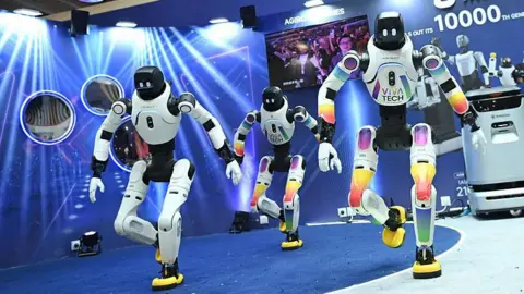 Bloomberg via Getty Images Three humanoid robots perform a dance routine.
