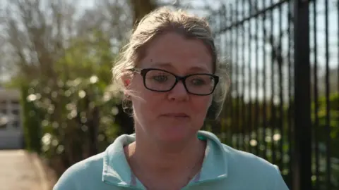 Family Candice Skinner is standing outside. She is wearing a light blue top and glasses with her hair tied back and she is looking worried.