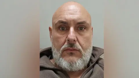 Police Scotland A man with a nose ring and brown eyes and a grey beard in a brown fleece top with the collar turned up