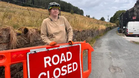 Local Democracy Reporting Service A warden next to a "road closed" sign, on an orange panel
