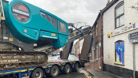 Shirley Henry / BBC The scene of the crash showing a blue Premiertrak R400 Jaw crusher on the back of a trailer which has apparently hit the top floor of a redbrick terrace house