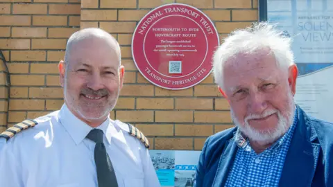 Two men stood in front of the red plaque 
