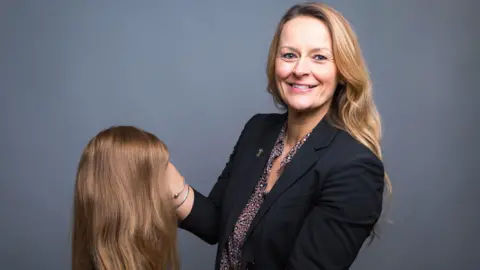 The Little Princess Trust Wendy Tarplee-Morris holding a long, blonde wig, which was made using donated hair