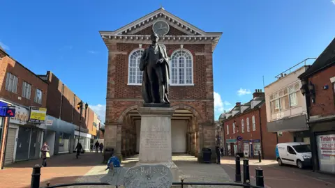 Tamworth Borough Council Tamworth Town Hall, a building with an open space and a series of columns underneath it. There is a statue of Sir Robert Peel in front of the building.