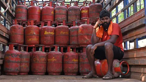 Getty Images A worker sitting on a LPG cylinder talks on his mobile phone in a truck inside a godown in Mumbai. 