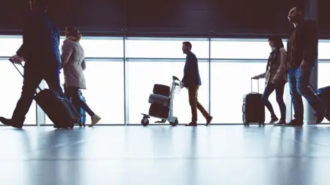 A stock photo of people walking through an airport holding luggage. 