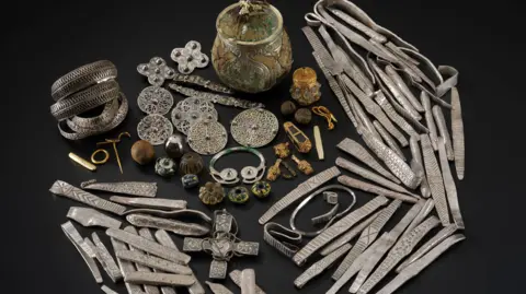 PA Media An image showing The Galloway Hoard spread over a black background. The metal artefacts include vases, brooches and jewellery, in silver and gold.