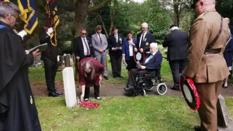 Washington History Society A group of people stand around a Commonwealth war grave. A woman is laying a wreath, and a soldier stands by holding one. 