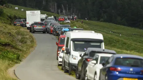 Getty Images A queue of cars parked along a narrow country road bordered by fields as tourists visit the Fairy Pools in Glenbrittle