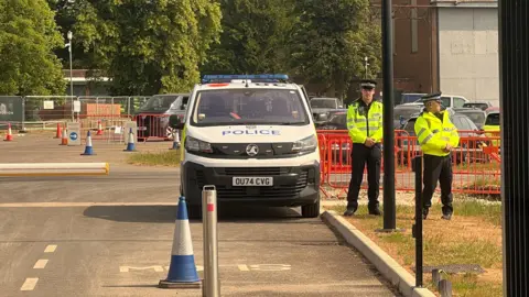 Two policemen and a police vehicle at the site. There are barriers and cones on the road behind them.
