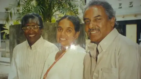 Nanda Malini posing for a photo, standing between two men