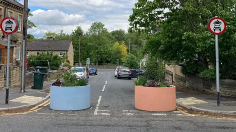 The top of terraced street with two concrete planters painted pale blue and pink blocking traffic from using it.