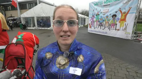 Callie-Ann Warrington smiling at the camera is wearing a marvel suit and glasses.