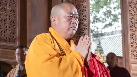 Shi Yongxin putting his palms together in a prayer position. He is wearing a yellow robe. File photo
