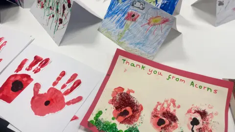 A selection of some of the hand made cards.  One has a poppy made out of a red handprint with a black centre, and another card next to it says "Thank you from Acorns".