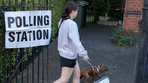 Getty Images A young woman entering a polling station in the UK while walking her dog.