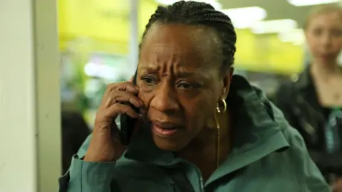 Studio Canal Marianne Jean-Baptiste in a green jacket and looking worried while using a mobile phone in Hard Truths