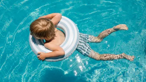Getty Images A child swimming in crystal blue water, he is in the middle of an inflatable ring.