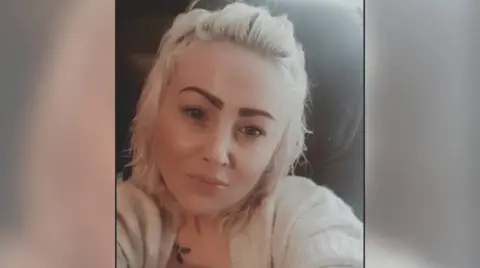 Facebook Selfie of Joanne Penney who has blonde shoulder-length hair tied back at the top and wearing a cream cardigan