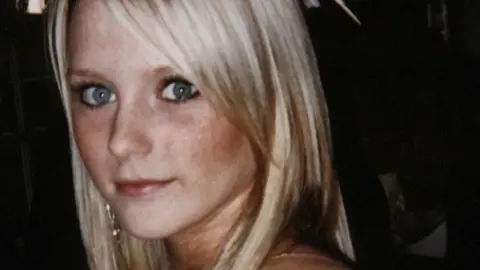 An 18-year-old girl with pale blonde hair and big eyes looking over her shoulder and smiling. She is dressed as for a night out.